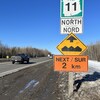Des enseignes en bordure de l'autoroute, en hiver. Un panneau indique que c'est la route 11 en direction nord. L'autre panneau indique que le chaussée est cahoteuse pour les 2 prochains kilomètres.