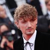 Un homme portant un veston noir et une chemise blanche regarde à sa gauche sur le tapis rouge du Festival de Cannes. 