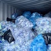Des sacs contenant des bouteilles de plastique vides sont empilés dans un conteneur maritime.
