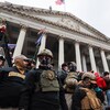 Des membres du groupes sur les marches du Capitole portant des vêtements de combat et des casques.