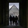 Quatre personnes devant la pyramide du musée du Louvre, à travers l'ouverture d'une porte.