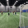 Des jeunes qui jouent au soccer sur un terrain intérieur.