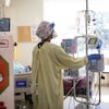 Un membre du personnel consulte de l'équipement médical tout près du lit d'un patient dans une chambre d'hôpital.