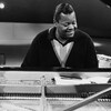 Dans un studio de télévision, Oscar Peterson assis à son piano dont le couvercle est relevé. À l'arrière-plan, on voit une caméra de télévision.