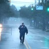 Un policier marche en plein milieu d'une rue, sous la pluie.