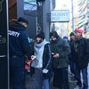 Photo de personnes en file sur le trottoir qui montrent leur carte d'identité à un agent de sécurité.