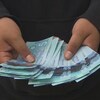 Une main tient des billets de 5 $ canadiens.