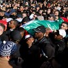Une foule transporte des corps enveloppés dans des drapeaux palestiniens.