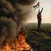 Un homme brandissant un drapeau palestinien près de pneus incendiés.