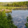 Le ciel bleu et quelques nuages se reflètent dans un petit lac bordé par une forêt de conifères dans le parc provincial de Nopiming, au Manitoba.