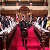 Le joueur de cornemuse sort de la chambre de l'Assemblée législative de la Colombie-Britannique, alors que les jeunes parlementaires sont debout.