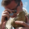 Un homme regarde dans une lunette une pierre qu'il tient dans sa main gauche.