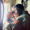 Un militaire dans un avion observe la mer à l'aide de jumelles.