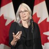 La ministre Patty Hajdu parle dans un micro devant des drapeaux canadiens.