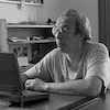 Pierre Foglia assis à un bureau, travaillant sur un ordinateur portable.
