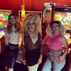 Un groupe de six drag queens posent devant des machines pinball.