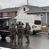 Quatre policiers dans la rue portant un uniforme d'allure miliaire et des fusils d'assaut ajustent leur équipement d'intervention.