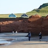 Des gens marchent sur la plage de la Dune-du-Sud, au pied de falaises de grès rouge.