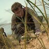 Un homme plante une herbe dans le sable d'une dune côtière.
