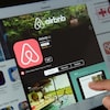 Un doigt touchant un écran sur lequel on voit la page d'accueil d'Airbnb.