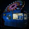 La lumière à l'intérieur d'un kisoke de limonade révèle deux jeunes travailleurs qui s'affairent à servir des clients. À l'arrière du kiosque, la grande roue, illuminé pour la nuit tourne à toute allure (1 septembre 2022).