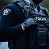 Plan rapproché de la poitrine d'un policier en uniforme couverte d'une veste noire décorée de l'emblème de la GRC, d'un walkie-talkie, d'une lampe de poche et d'un gilet pare-balles sur lequel le mot « Police » est écrit.