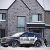 Un policier dans une voiture de police stationnée devant une résidence.