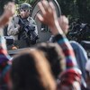 Un policier tient une arme face à des manifestants.
