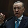 Le président turc Recep Tayyip Erdogan parle dans deux micros, devant un drapeau turc.
