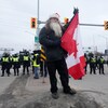 Un homme brandit le drapeau canadien devant les policiers chargés de déloger les manifestants qui bloquent l'accès au pont Ambassador le 12 février 2022.