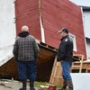 Deux hommes devant une grosse cabane à l'envers après avoir été renversée par un ouragan.