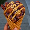 Des morceaux de poulet croustillants glacés à la gelée de raisin, agrémentés d'une savoureuse sauce satay à la cacahuète, sont servis dans un cône de gaufre.