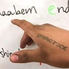 Une main montre du doigt un mot écrit dans une langue autochtone sur un tableau blanc. 