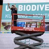 Une travailleuse montée dans un échafaudage, au Palais des congrès de Montréal, devant une murale annonçant la COP15 sur la biodiversité.