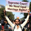 Un homme tient une pancarte en appui au mariage homosexuel, entouré de ballons arc-en-ciel.