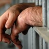 Les mains d'un détenu à l'extérieur des barreaux d'une cellule de prison. 