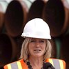 Rachel Notley qui porte un casque de construction devant des tuyaux de pipeline.