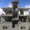 Des Palestiniens se tiennent debout dans un immeuble dont la façade et une partie des murs ont complètement été détruits.