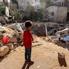 Un enfant est debout devant les débris d'un bâtiment.