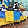 Des dizaines de personnes alignées dehors en hiver dans le froid tiennent une longue bannière jaune et bleu et une affiche avec le message « We Stand With Ukraine ».