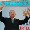 Le président Erdoğan, les deux bras en l'air, est debout sur une scène.