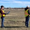 Deux personnes observent au loin un drone se trouvant sur un terrain. 