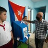 Encadré par deux adolescents, un Cubain dépose un bulletin de vote dans une urne.