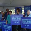Un groupe de personnes brandissant des pancartes sur lesquelles on peut lire «Donate this much space».