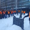 Des personnes portant des gilets oranges et des manteaux d'hiver se tiennent debout dans un parc au centre-ville de Montréal.