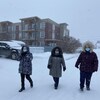 Trois femmes marchent à l'extérieur l'hiver devant une résidence.