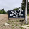 Une voiture roule sur une route au bord de laquelle on aperçoit une plaque avec un message en anglais donnant des indications sur la façon de se plaindre de son état.