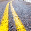 Plan rapproché de la ligne jaune peinte au milieu d'une route bordée d'une mince couche de neige.