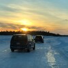 Deux véhicules s’engagent sur la route de glace au coucher du soleil.