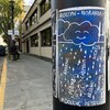 Une affiche collée sur un poteau illustre un nuage qui sourit. Les mentions de plomb, cadmium, nickel, arsenic et souffre s'ajoutent aux gouttes d'eau. La mention « Douche rebelle » est aussi ajoutée.